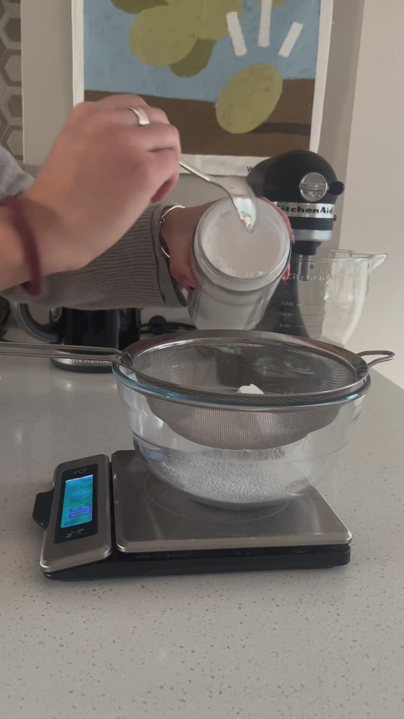 Video showing Chef baking French Financiers using flour, sugar, coffee glaze and Butter and Bright Silicone Tube Cylinder six cavity mould. Airy light filled workspace with contemporary fixtures. Cakes are finished with coffee glaze stirred in Butter and Bright Cobre resin Coupe bowl and topped with walnuts.